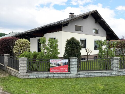 Einfamilienhaus mit gepflegtem Garten und modernisierter Fassade, an dessen Grundstücksmauer ein bösch-Bauschild auf die Installation einer Wärmepumpe hinweist. | © Walter Bösch GmbH & Co KG