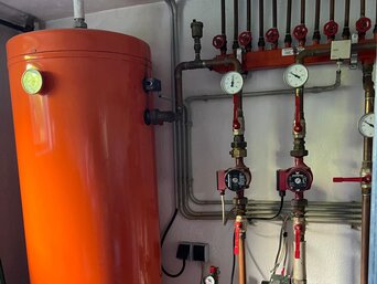 Alter, senkrecht stehender Warmwasserspeicher mit Rohrleitungen und Armaturen in einem Technikraum – vor dem Austausch durch einen energieeffizienten Speicher von bösch. | © Walter Bösch GmbH & Co KG