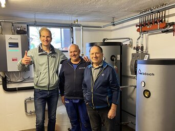 Der Hausbesitzer steht gemeinsam mit zwei Fachleuten in einem Heizraum neben dem neuen bösch Wärmepumpensystem und zeigt sich erfreut über die erfolgreiche Inbetriebnahme. | © Walter Bösch GmbH & Co KG