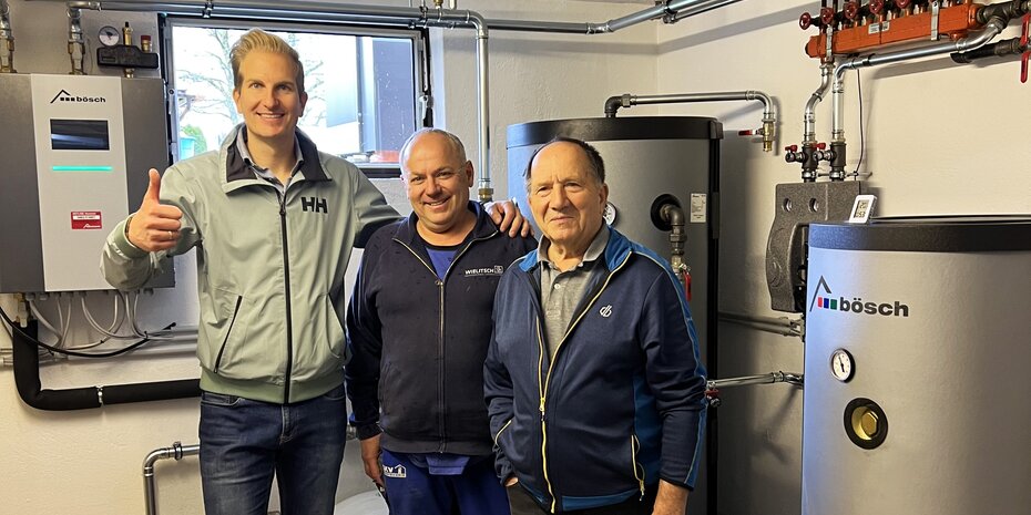 Der Hausbesitzer steht gemeinsam mit zwei Fachleuten in einem Heizraum neben dem neuen bösch Wärmepumpensystem und zeigt sich erfreut über die erfolgreiche Inbetriebnahme. | © Walter Bösch GmbH & Co KG