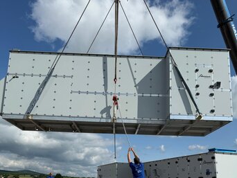 Kran positioniert ein vormontiertes Lüftungsgerät auf der vorbereiteten Dachkonstruktion des TEST-FUCHS Aerospace Campus.
