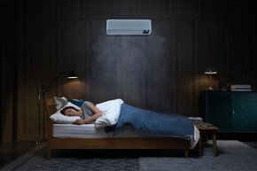 Frau schläft in dunklem Schlafzimmer, über dem Bett hängt eine Samsung Klimaanlage